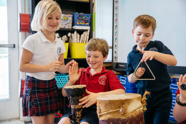 three students make music with drum and triangle