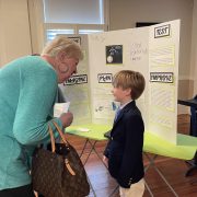 CDS Invention Convention student with a presentation board talking to a grandparent